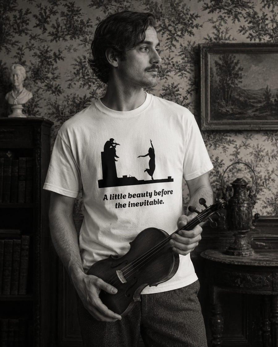 Black-and-white photograph of a man holding a violin in an old room, wearing a shirt printed with a violinist, a dancing woman and the words: a little beauty before the inevitable.